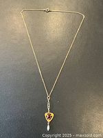 Full view of necklace laid flat showing gold chain and triangular pendant with red stone and pearl