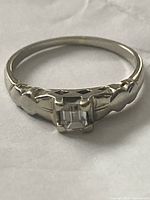 Front view showing emerald-cut diamond and Art Deco shoulder detailing