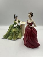 Photo showing both Royal Doulton figurines, one in red dress and one in green dress seated