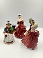 Three Royal Doulton ceramic figurines - Balloon Lady, Vivienne, and Autumn Breezes together from front with white background.