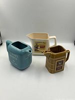 Photo showing all three vintage ceramic whiskey water pitchers including Logan, Johnnie Mac, and Thorne's in different colors and shapes.