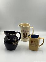 Three vintage Scotch whiskey branded ceramic water pitchers together - Buchanan, Grants, and B+L pitchers.