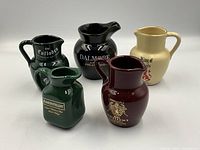 Group photo of 5 small water pitchers themed after Scotch whiskey brands, different colors and logos visible