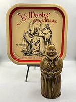 Photo showing the Ye Monks Scotch Whisky ceramic decanter shaped as a monk and the metal serving tray behind it on a stand.