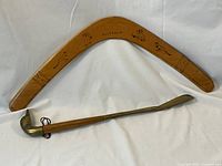 Photo showing large wooden boomerang with wildlife engravings and brass duck head shoe horn below it.