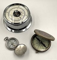Top view of the lot showing all three items: a Chrome Airguide barometer, a brass compass with engraving, and a nickel compass with cover open.