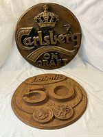 Two round carved wooden beer advertising signs, Carlsberg and Labatt's 50 Ale, side by side against white backdrop