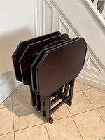 Stand with four folding tray tables stacked inside, shown from an angle.