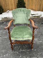 Front view of the hand carved wooden armchair with sage green velvet upholstery showing seat, backrest and armrests.