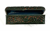 Side view of the black and red hinged box showing intricate carved or molded designs on the outer surface and the open lid displaying blue enamel interior.