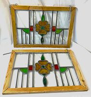 Two stained glass window panels stacked, showing detail and frame sides with hanging chains.