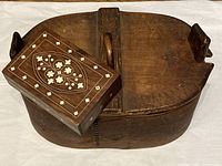 Top view showing the smaller box resting on the larger oval box with handle and the vintage wooden surface.