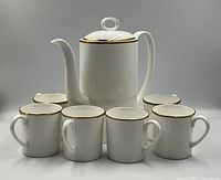 Front view of the coffee set showing one tall coffee pot and six cups with gold rim accents
