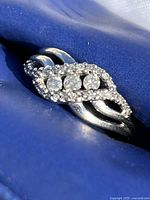 Front-facing view of ring showing three round center stones and surrounding halo of accent stones on twisted band