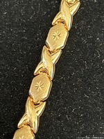 Close-up photo showing starburst engraving on hexagonal links and orchid-shaped links in a repeating pattern of yellow gold bracelet.