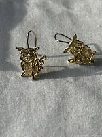 Two gold earrings shaped like Pikachu, shown lying on a gray fabric.