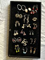 Top-down angled photo capturing the entire set of earrings displayed on a black velvet tray, showing various earring styles and colors.