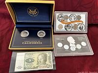 Top view showing Great State of California coin set case with two coins, American Nickel Coin Collection set in plastic holder, 1943 Steel Cents set, and vintage 5 Deutsche Mark bill.