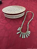 Photo showing the jade necklace alongside the inlaid jewelry box on a red cloth background.