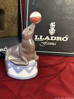 Front angle view of Lladro seal balancing a red and white beachball on nose, with original Lladro Fauna box in background.