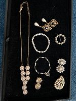 Lot contents showing necklace, three pairs of earrings, two bracelets, and two brooches arranged on black surface.