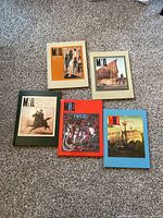 Top-down view of 5 hardcover military history journals with assorted cover colors and historical scenes.