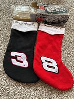 Photo showing pair of NASCAR Christmas stockings: black with number 3 and embroidered 'Dale Earnhardt' on cuff, and red with number 8 and 'Dale Earnhardt Jr.' embroidered on cuff, placed on carpet.