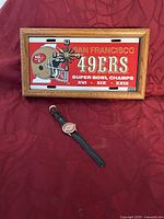 Photo of the framed San Francisco 49ers Super Bowl championship clock and the wrist watch on red fabric.