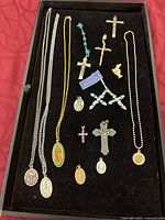 Full set of 15 assorted religious jewelry items arranged on black cloth including necklaces, crosses, pins, and religious medals.