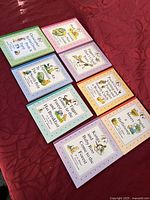 Shows all eight books laid out in two rows on a red fabric. The books are pastel pink, orange, blue, green, purple, and pink. Covers include titles and classic illustrations of Winnie the Pooh characters.