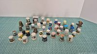 Wide view of 41 unique collectible thimbles arranged in rows on a blue textured surface, showing various souvenir landmark designs.