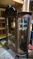 Front view of the antique wooden curio cabinet showing carved wood detailing on top and glass panels in front and sides.