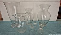 Front view of the glass collection showing three vases, one pitcher, and four small suction cups arranged on a blue surface with a neutral background.