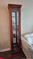 Front view of a tall, narrow wood and glass display cabinet in mahogany finish showing multiple glass shelves and glass door with metal handle