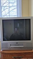 Front view of the JVC CRT TV and VHS player unit on wooden surface, screen off reflecting background.
