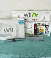 Photo of Nintendo Wii console box with one Wii Remote controller, sensor bar with stand, Wii Fit Balance Board box, and four Wii game cases.