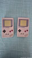 Two original gray Nintendo Game Boy DMG-01 handheld consoles side by side on fabric background.