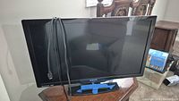 Philips 32-inch LED-LCD TV front angled view with HDMI cable draped over screen and blue tape on stand base.