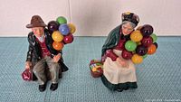 Front view of male and female Royal Doulton balloon seller figurines seated with colourful balloons