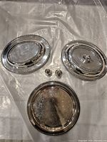 Lot showing three silver plated brass items: two oval dishes (one with handle, one missing handles) and one round plate, plus a pair of small salt and pepper shakers.