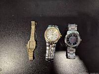 Three watches laid out on black surface: Pulsar gold-plated women's, Citizen Eco-Drive men's, Tommy Hilfiger men's