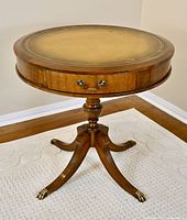 Full view of circular mahogany drum table with turned pedestal and brass claw feet