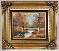 Front view showing the oil painting on canvas of a fall forest with a meandering stream framed in an ornate gilded wooden frame with floral corner decorations.
