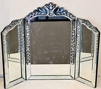 Front view of the three-sided vanity mirror showing the central panel and open side wings with etched leaf pattern on the glass and beveled edges.