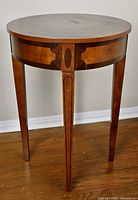 Full view of the round drum side table showing top, apron, and three tapered legs with inlay detail.