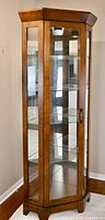 Front view of tall hexagonal corner curio cabinet showing walnut wood frame, glass door, and mirrored back with shelves inside.