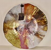 Full front view of a round decorative glass plate with an irregular edge, showing a multicolor abstract design with metallic gold, bronze, white, and pink tones.