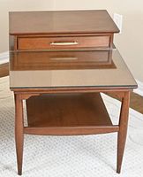 Front view showing stepped tabletop, drawer front with brass handle, glass inset and lower shelf