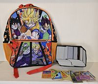 Front view of Dragon Ball backpack featuring Dragon Ball Z characters and Pokemon card tin filled with cards, with some cards laid out in front.