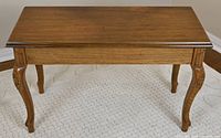 Front angle view of the piano bench showing carved cabriole legs and walnut wood top with some wear spots.